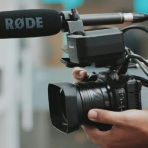 Close-up of hands holding a professional video camera with a RØDE microphone attached.